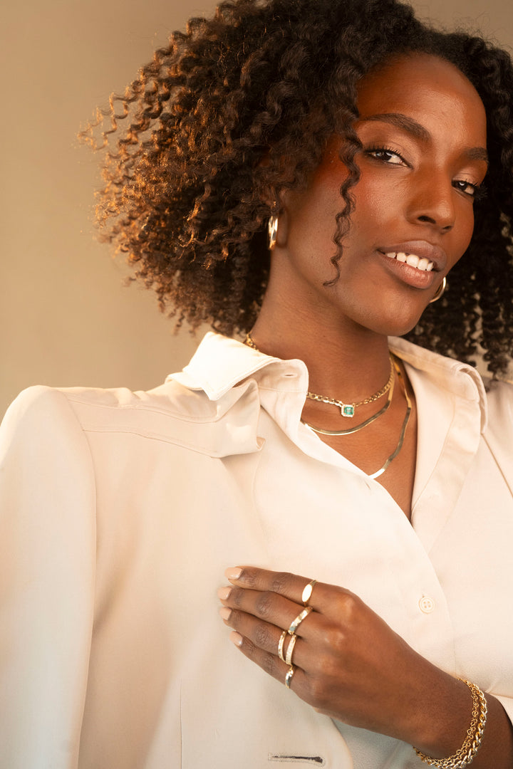 A black woman with curly hair wearing a white shirt and gold jewelry, showcasing rings and necklaces.