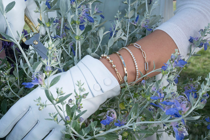 A girl's hand adorned with multiple spring-style bracelets, holding one bracelet amidst a field of blue flowers.